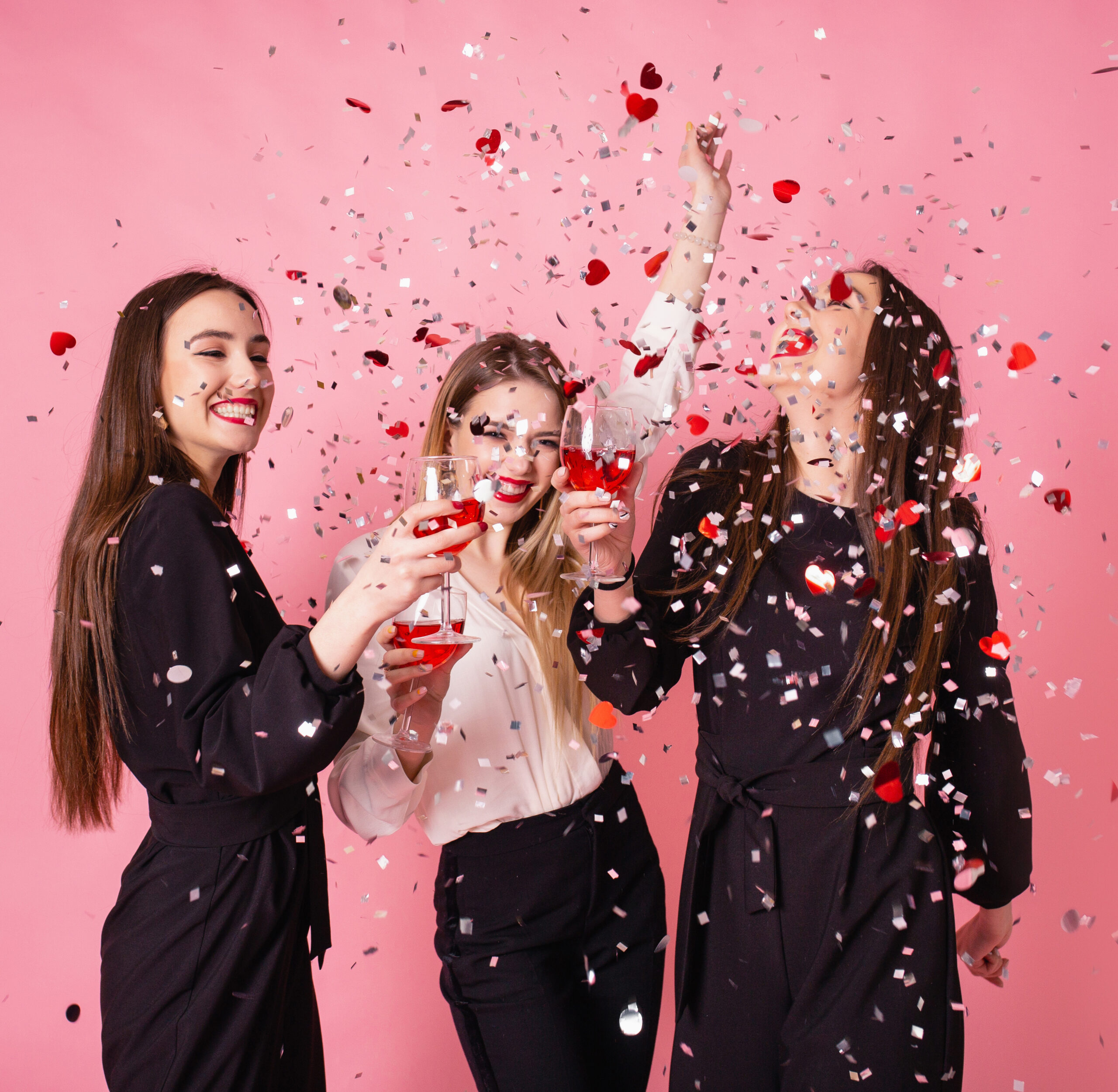 Girls posing and smiling on pink background, cheerful emotions, bright makeup, red lips, indoors party, wearing black and white stylish evening outfits.